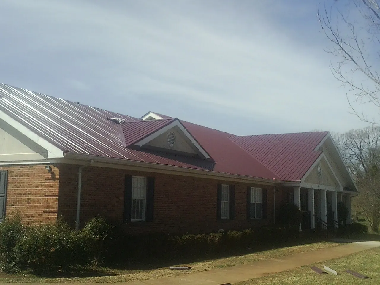 Red metal roof with gabled entries on a long brick building, from a Hail Damage Roof Repair job in Morgantown